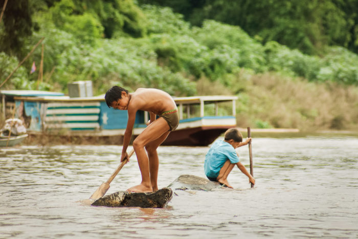 two Kids on a branch paddling in the mekong river in Laos taken by Milie Del