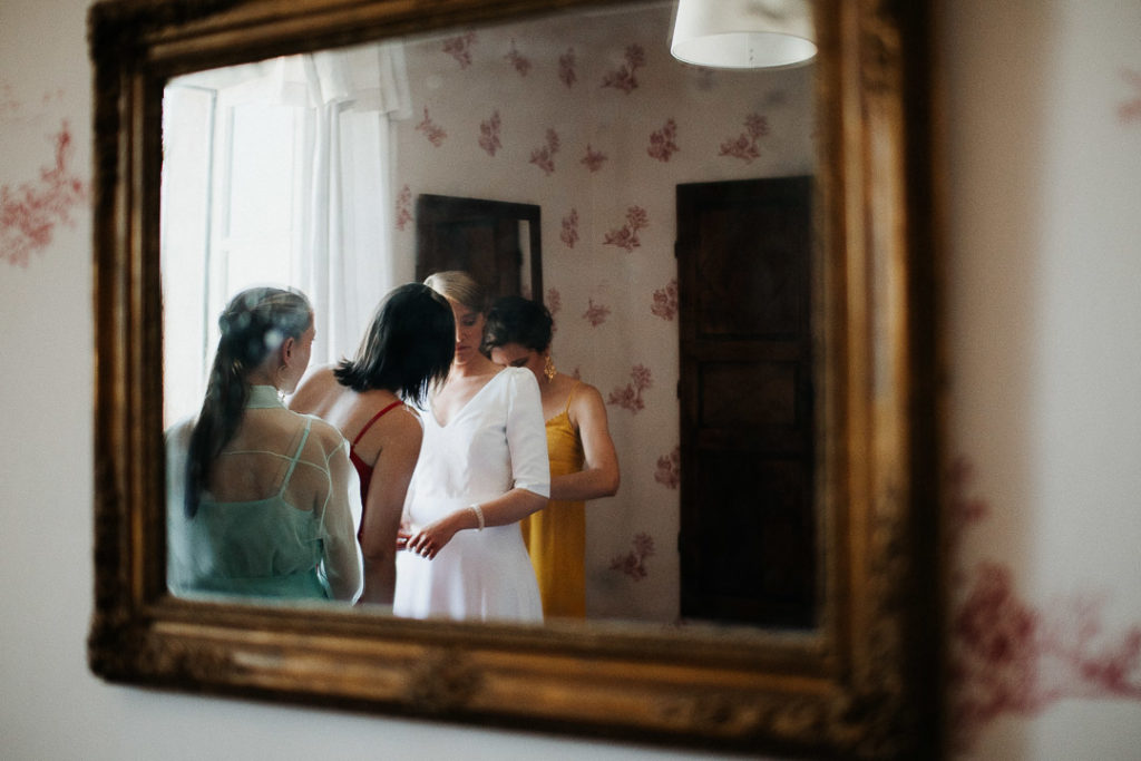Bridemaids in the mirror helping the bride
